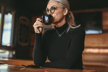 Thoughtful senior woman sitting at cafe drinking coffee. Businesswoman in casuals drinking a cup of coffee. - JLPSF23933