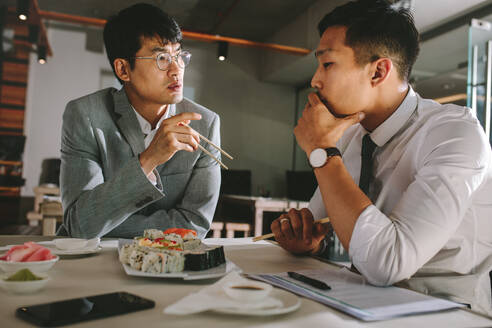 Two business professionals discussing working over a lunch at restaurant. Businessmen talking with colleague while having food at restaurant. - JLPSF23935