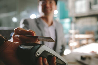 Close up of businessman paying with contactless credit card with nfc technology at restaurant. Focus on man holding his credit card above the card reading machine. - JLPSF23944