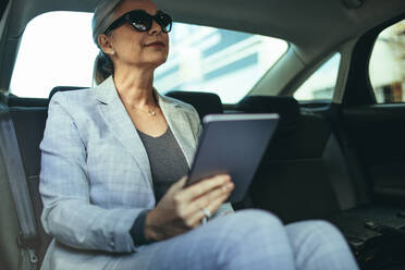 Female entrepreneur travelling to office in a luxurious car sitting on backseat with digital tablet. Senior businesswoman in car with tablet pc. - JLPSF23971