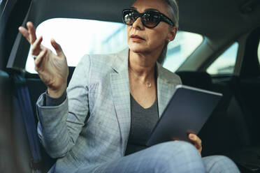 Beautiful mature businesswoman sitting on back seat of a car and looking outside the window. Female business executive travelling by a car. - JLPSF23972