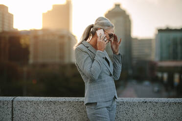 Portrait of senior businesswoman standing on the bridge outdoors and talking on mobile phone. Mature business professional talking on cellphone outdoors on city street in evening. - JLPSF23989