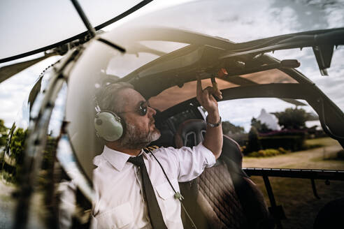 Pilot with headset starting the controls in the private helicopter. Helicopter pilot sitting in the cockpit. - JLPSF24024