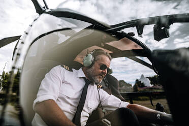 Male pilot operate switches of helicopter system prior to departure. Pilot sitting inside helicopter cockpit. - JLPSF24025