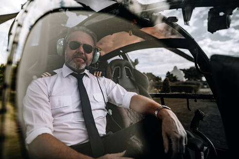 Portrait of mature male pilot with headset sitting in the private helicopter. Pilot sitting in the cockpit of a helicopter. - JLPSF24026