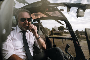 Happy helicopter pilot with headset in the helicopter. Male pilot talking on the headset in the cockpit of a helicopter. - JLPSF24027