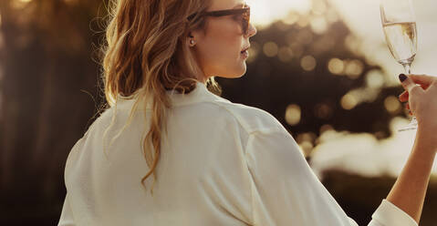 Pretty woman looking at a glass of wine outdoors. Rear view of female looking at her wine glass. - JLPSF24046