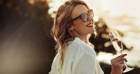 Smiling woman in sunglasses drinking wine. Beautiful female model with a glass of wine outdoors. - JLPSF24049