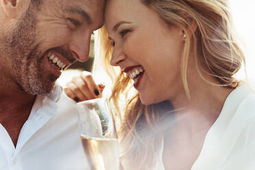 Close up of smiling couple with their heads touching and laughing. Loving couple with wine enjoying each others company. - JLPSF24053