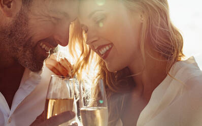 Close up of a young couple with their heads together holding a glass of wine and smiling. Romantic couple with wine outdoors. - JLPSF24054