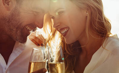 Close up of a romantic couple with their heads together holding a glass of wine. Couple with wine smiling outdoors. - JLPSF24055