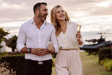 Handsome man with his beautiful girlfriend walking together outdoors. Beautiful couple walking outdoors with a helicopter at the back. - JLPSF24058