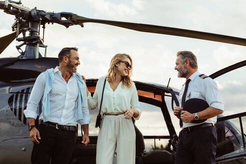Smiling couple alighted from a private helicopter talking to the pilot. Couple getting off a private aircraft with mature pilot. - JLPSF24064