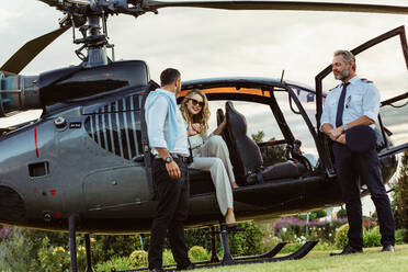 Beautiful woman getting down the helicopter with the help from her boyfriend. Couple disembarking their helicopter with pilot standing by. - JLPSF24065