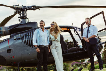 Beautiful couple alighted from a private helicopter and looking at a view with pilot standing by. Couple standing by a private aircraft with pilot. - JLPSF24066