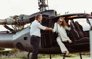 Pilot holding hand of a woman getting off the helicopter. Wealthy young woman traveling by her helicopter. - JLPSF24068
