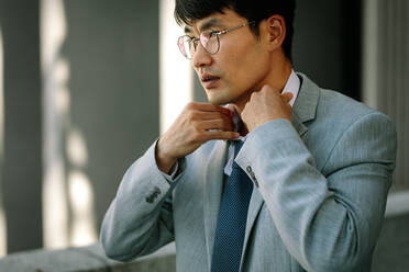 Businessman adjusting his necktie. Asian business professional in suit adjusting his tie. - JLPSF24079