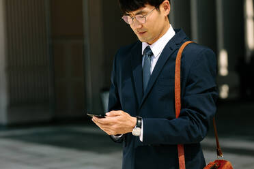 Asian businessman walking outdoors using mobile phone. Korean man walking and using a smart phone outdoor. - JLPSF24081