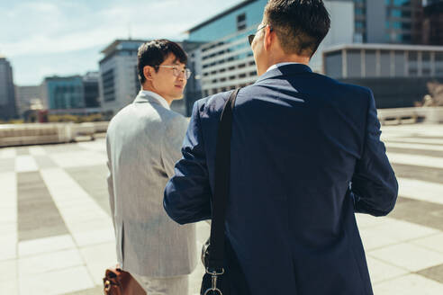 Rear view of two business people walking and talking together outdoors in the city. Two businessmen talking and walking in the city. - JLPSF24088