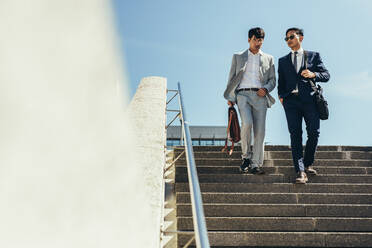 Two business people walking down stairs. Korean business men talking and walking down the steps. - JLPSF24091