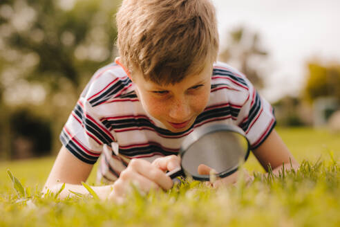 Young caucasian boy exploring garden with his magnifying glass. Cute boy looking through magnifying glass at the grass. - JLPSF24120