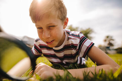 Boy looking through magnifying glass on a sunny day. Caucasian boy exploring garden with his magnifying glass. - JLPSF24122