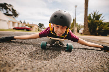 Boy with helmet lying on his skateboard outdoors on road. Happy and smiling boy lying on his skateboard and skating on the road. - JLPSF24128