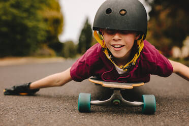 Small boy lying on his skateboard using his hands to guide while riding outdoors. Funny boy with helmet lying on skateboard. - JLPSF24130