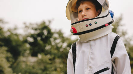 Small boy pretending to be an astronaut wearing a space suit and helmet standing outdoors. Boy playing to be an astronaut with space helmet and suit. - JLPSF24134