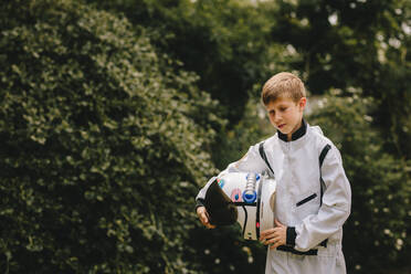 Boy wearing space suit holding a helmet walking outdoors. Cute boy in space suit and helmet playing astronaut in playground. - JLPSF24137