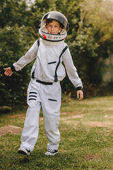 Kid playing in astronaut suit outdoors. Boy pretending to be an astronaut, wearing space suit and helmet. - JLPSF24139