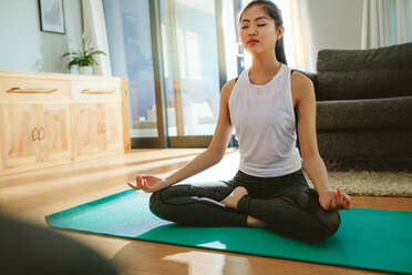 Fit junge Frau meditiert in Lotus-Pose zu Hause. Schöne Frau macht Yoga-Übung im Haus. - JLPSF24150