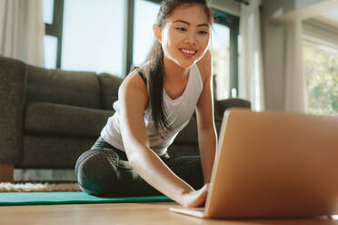 Eine Frau in Sportkleidung sitzt auf dem Boden und sieht sich ein Trainingsvideo für ihr Workout an. - JLPSF24154