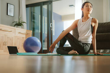 Gesunde Frau sitzt auf Übungsmatte und macht Yoga. Asiatische Frau übt Yoga für eine gute Gesundheit. - JLPSF24162