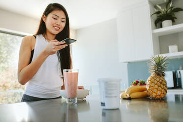 Junge asiatische Frau fotografiert ein gesundes Frühstück mit einem Handy. Frau fotografiert ihr nahrhaftes Essen auf der Küchentheke am Morgen. - JLPSF24173