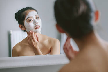 Woman with facial mask in front of bathroom mirror. Beautiful female doing beauty treatment in bathroom. - JLPSF24180