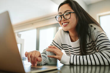 Young woman sitting at tablet with coffee surfing the net on laptop computer. Asian female using laptop at home in morning. - JLPSF24195