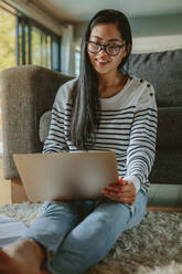 Woman sitting on floor and leaning to sofa using laptop. Female student studying at home. - JLPSF24200