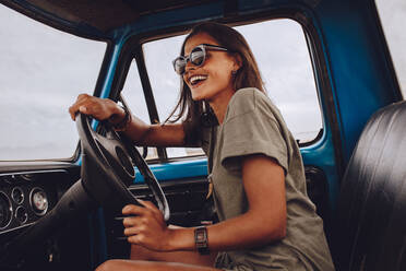 Porträt einer jungen Frau, die sich beim Autofahren amüsiert. Fröhliche Frau, die mit einem alten Lastwagen auf eine Spritztour geht. - JLPSF24227