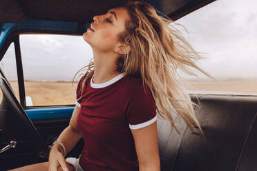 Side view of young woman sitting in the car and relaxing. Woman on road trip taking a break after a long drive. - JLPSF24241