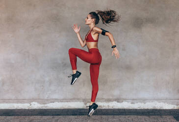 Sportswoman jumping and stretching. Full length of healthy female exercising and jumping outdoors. - JLPSF24293