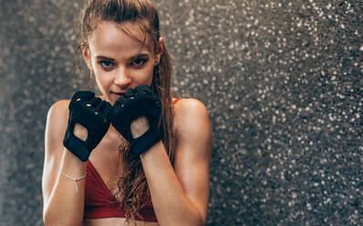 Young woman standing in fighting stance. Female boxer exercising outdoors against grey wall. - JLPSF24302