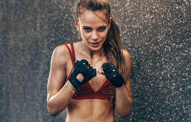 Frau mit Handschuhen, bereit zum Kampf. Boxerin beim Training im Freien vor einer grauen Wand. - JLPSF24303