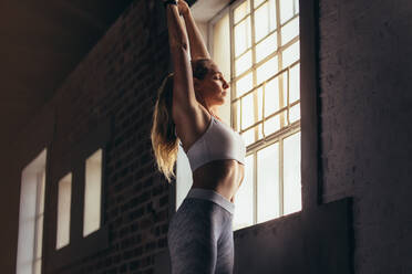 Fit woman stretching while standing by window at gym. Young female doing stretching workout at fitness club. - JLPSF24318