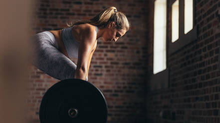 Healthy young woman lifting a barbell with heavy weights at the gym. Fit female athlete exercising with heavy weights at cross training gym. - JLPSF24322