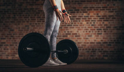 Low section view of woman standing at fitness club with heavy weight barbell no floor. Woman doing weight lifting workout at gym. - JLPSF24325