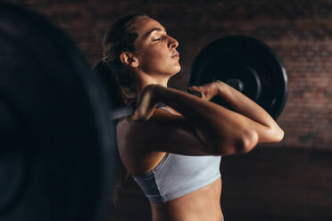 Junge Frau beim Hanteltraining mit schweren Gewichten in einem Fitnessclub. Frau in Sportkleidung beim Gewichtheben im Fitnessstudio. - JLPSF24328