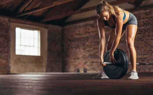 Weibliche Athletin bereitet Gewichte für das Training im Fitnessclub vor. Muskulöse Frau befestigt den Clip an der Langhantel. - JLPSF24331