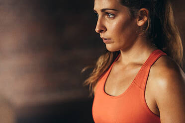 Nahaufnahme einer jungen Frau in orangefarbenem Sport-BH, die nach dem Training eine Pause einlegt. - JLPSF24333