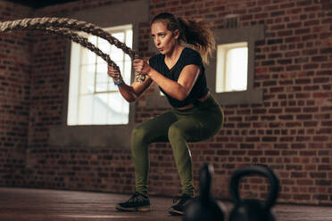 Fitness Frau mit Kampfseilen für die Ausübung. Weibliche Arbeit mit Kampfseilen an Cross-Training Fitnessstudio. - JLPSF24336